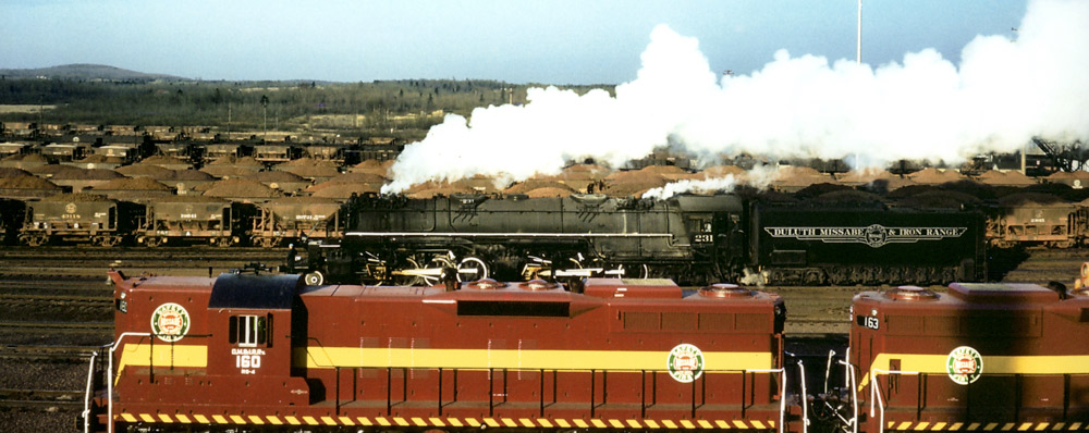 Road-switcher diesel locomotive in foreground, articulated steam locomotive in background