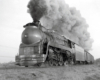 Streamlined steam locomotive hauling a passenger train emitting a large smoke plume.