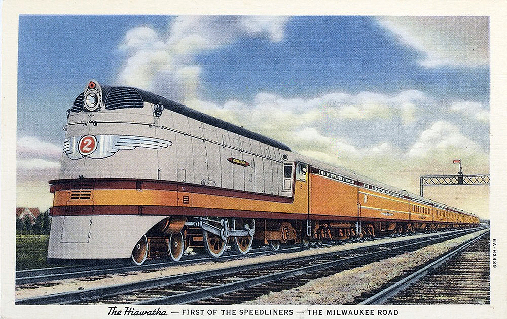 Image of a gray-and-orange steam locomotive at the head of a passenger train.