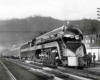 A streamlined steam locomotive at the head of a passenger train.