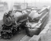 Two steam locomotives, side-by-side. The one on the right is streamlined.