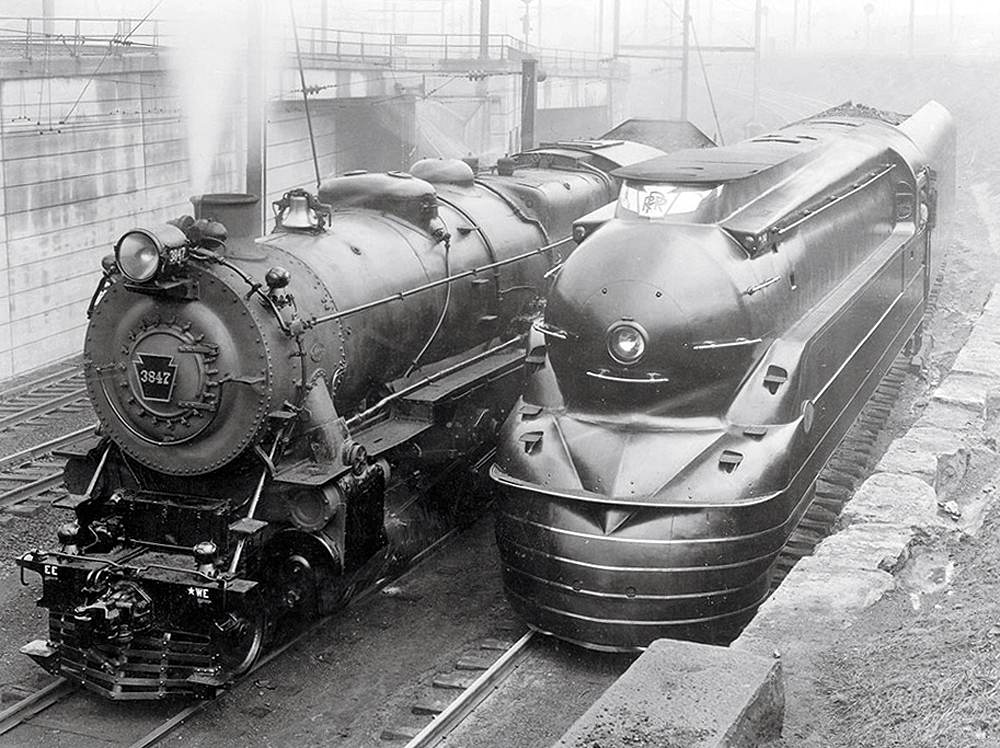 Two steam locomotives, side-by-side. The one on the right is streamlined.