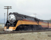 An orange-and-black steam locomotive at the head of a passenger train.