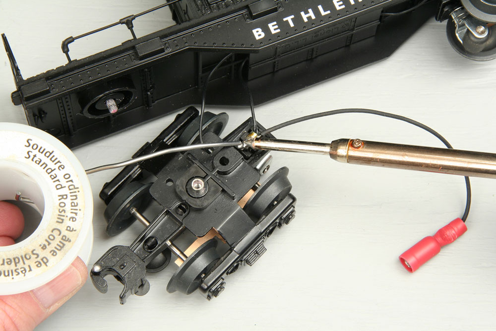 Soldering wire with female connector to metal contact for pickup roller on caboose truck that has been unscrewed from body.