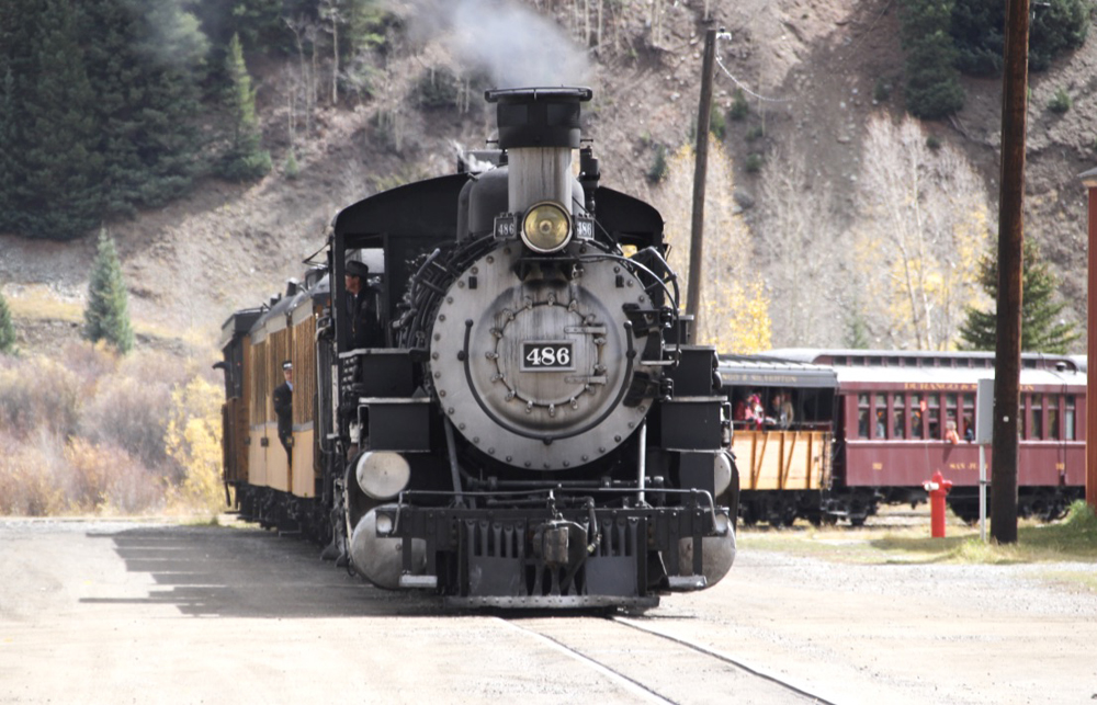 Steam locomotive leads train onto dirt street