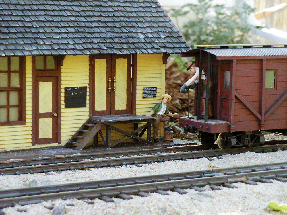 A caboose passes the station on a garden railway.