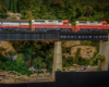 Three red-and-white Western Maryland diesels lead their train onto a girder bridge spanning a road and a creek