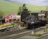 A restored vintage steam engine pulls up to a station to be greeted by railfans and a mariachi band