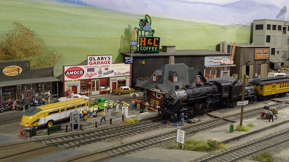 A restored vintage steam engine pulls up to a station to be greeted by railfans and a mariachi band