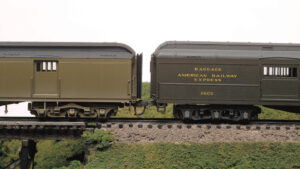 Two olive green HO scale heavyweight passenger cars are compared for height.