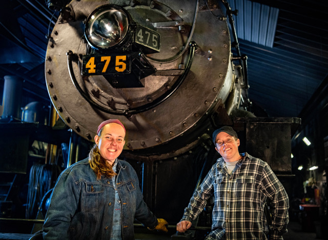 Two women railroaders pose near the pilot of a steam locomotive.