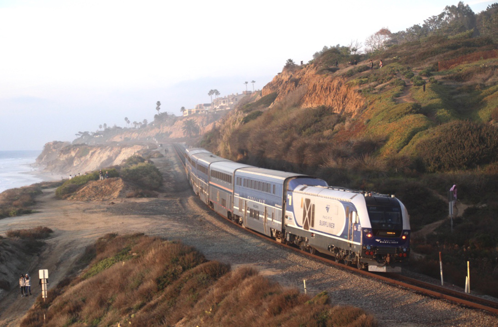 Amtrak passenger train moves along tracks on coastal bluff in light fog.