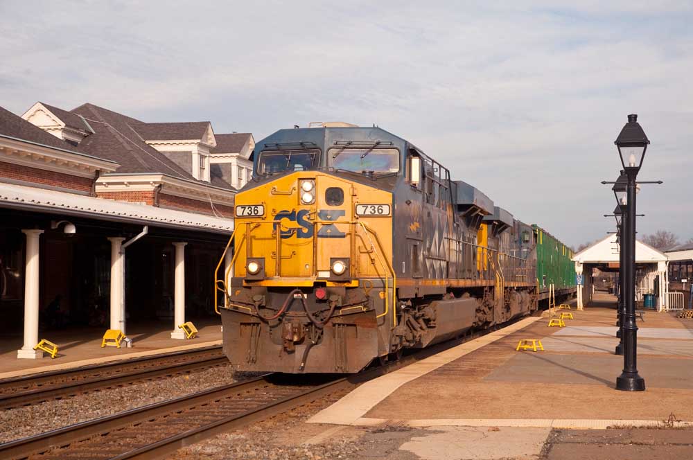 Yellow and blue diesel powers freight train past brick station