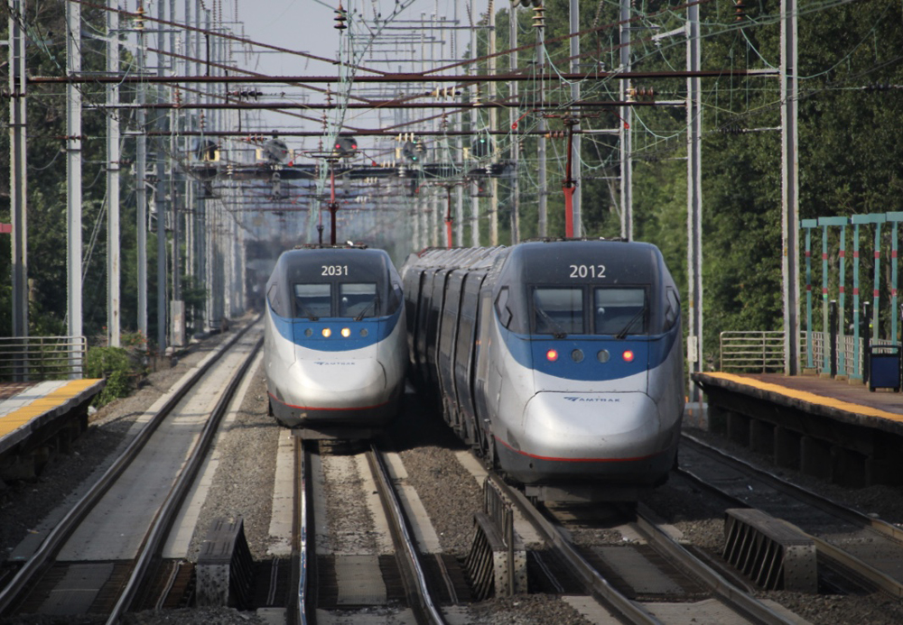 Two Amtrak Acela trains under catenary wire on a multi-track mainline.