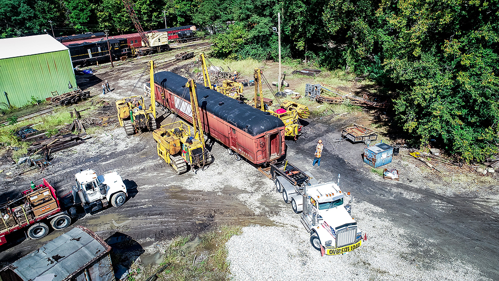 Cranes and a truck moving a piece of railroad equipment.