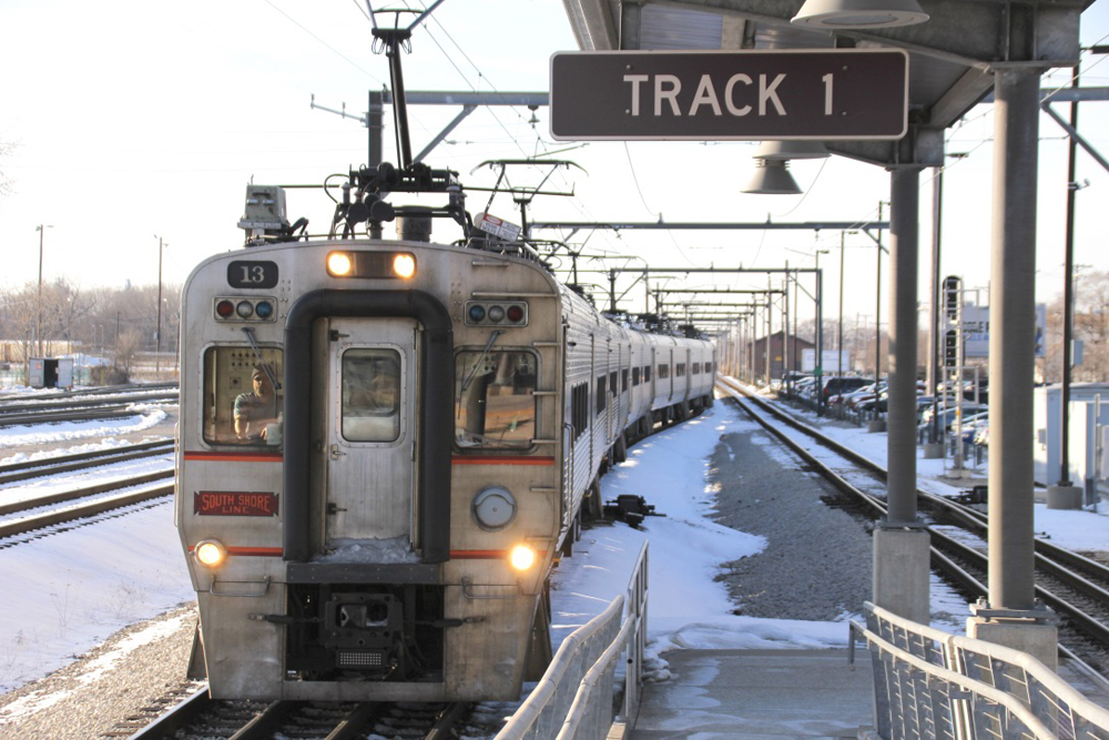 An electric passenger train pulls into a station in a snowy scene.