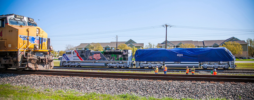 Locomotive under tarp, pulled by another locomotive