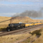 A Big Boy locomotive leads a yellow passenger train through the Great Plains.