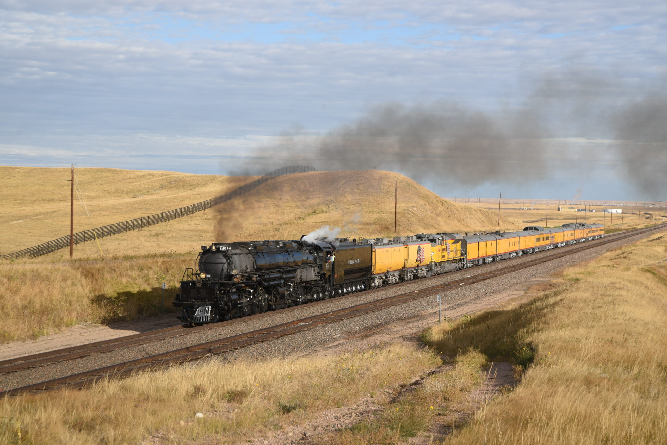 A Big Boy locomotive leads a yellow passenger train through the Great Plains.