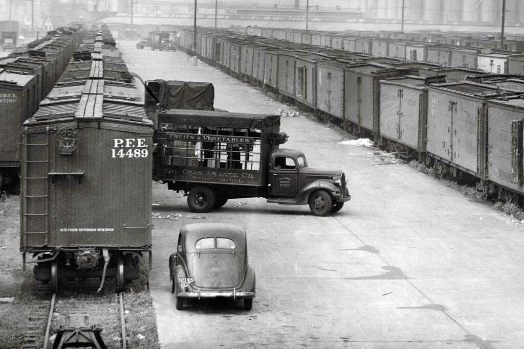 Trucks back up to railroad freight cars to load goods