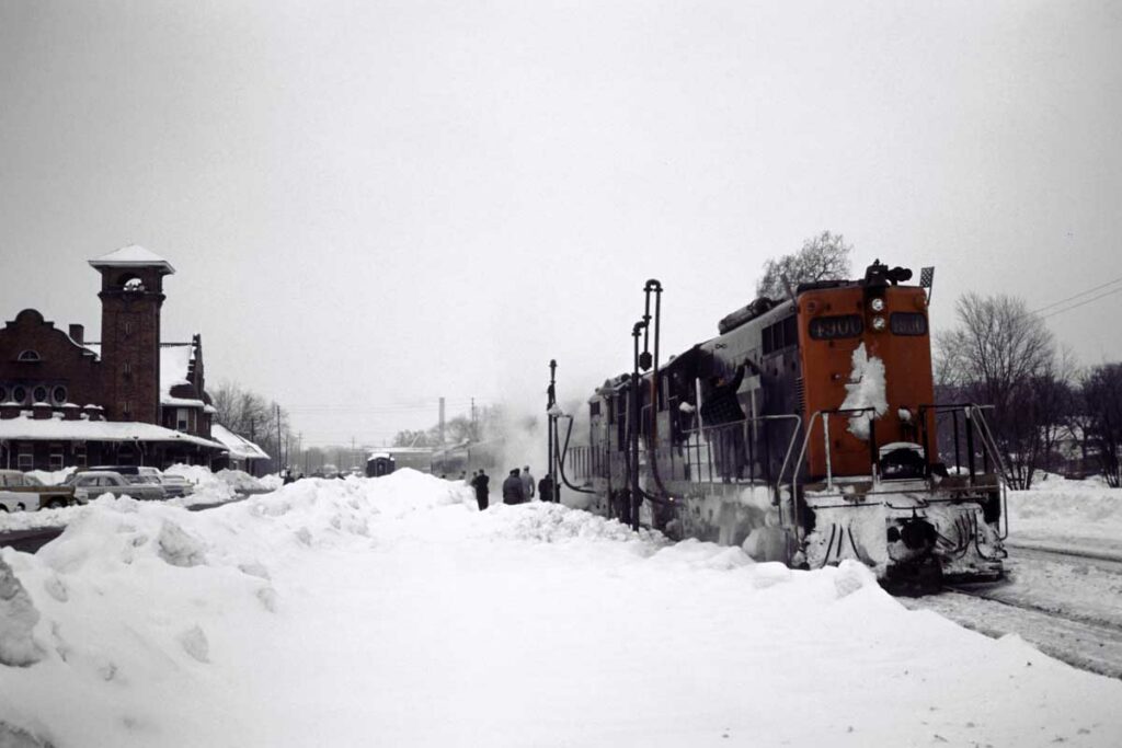 Diesel locomotives with passenger train at brick station in snow