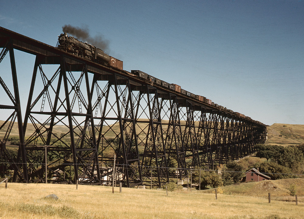 Steam locomotive leading freight train over long trestle