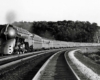 Streamlined steam locomotive and passenger train on a gentle curve.