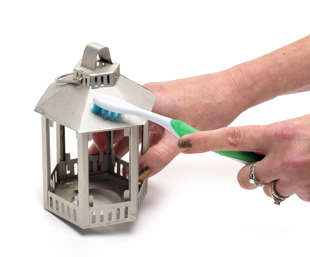 Hands using an old toothbrush to clean lantern tealight holder.