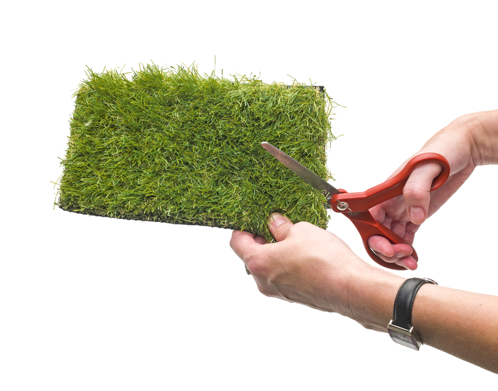 Scissors cutting a piece of outdoor carpet.