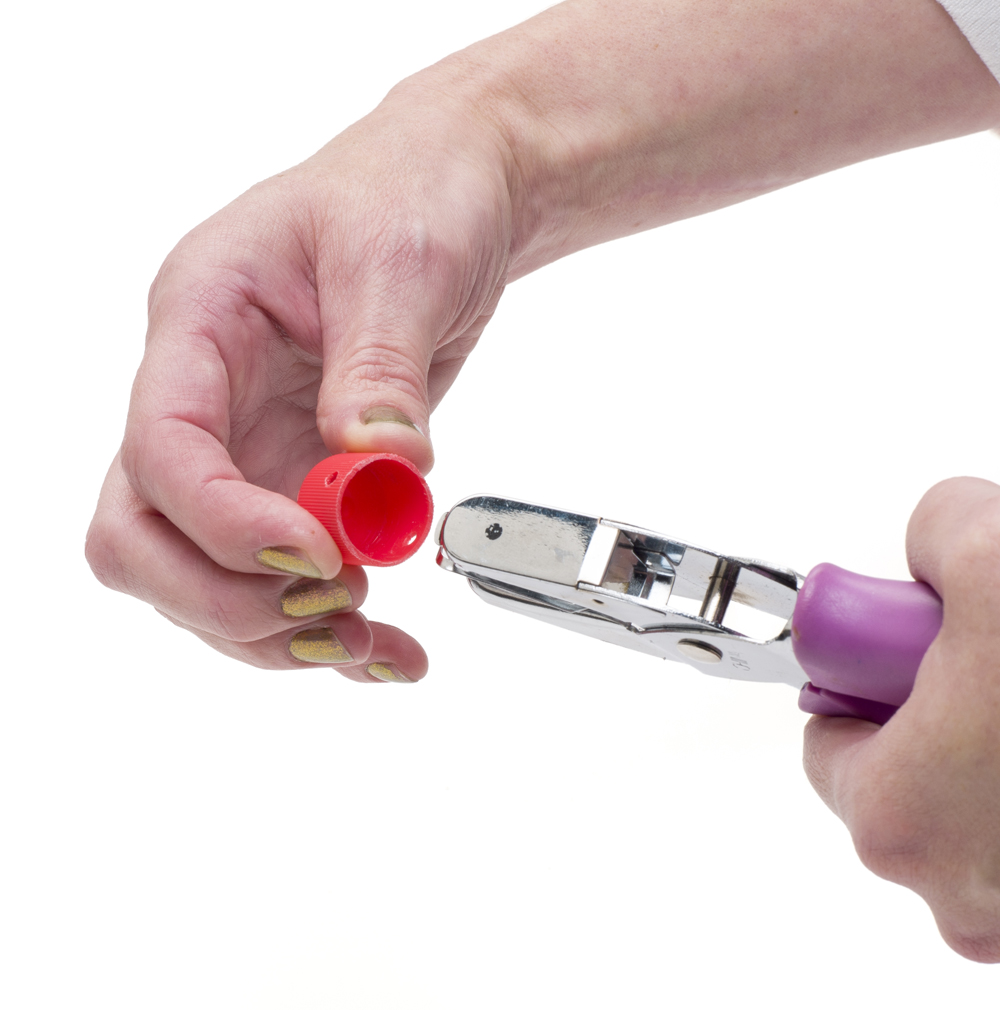 Hands using a hole punch to cut hole in the side of a small cap