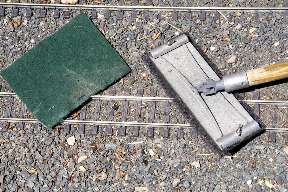 A drywall sander with a green Scotch-Brite pad next to gauge-1 track.