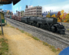 Union Pacific Big Boy moving left to right prepares to leave yard with mixed freight train, dirt rpad in foreground, industrial buildings in background