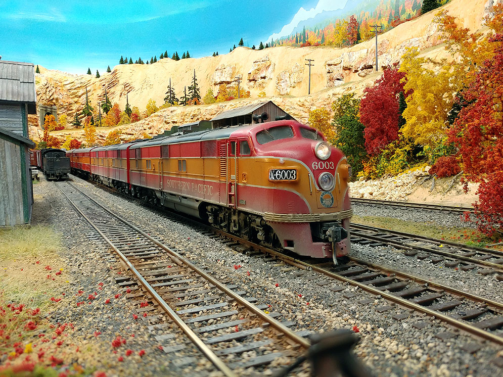 EMD E7A pulls red and orange Southern Pacific Daylight along two-track main line through western mountain scene in fall