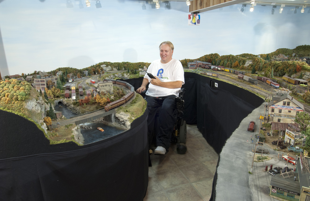 A man sitting in a wheelchair operates his HO scale model railroad