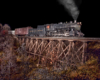 A steam locomotive is dramatically lit from the side as it crosses a wood trestle at night