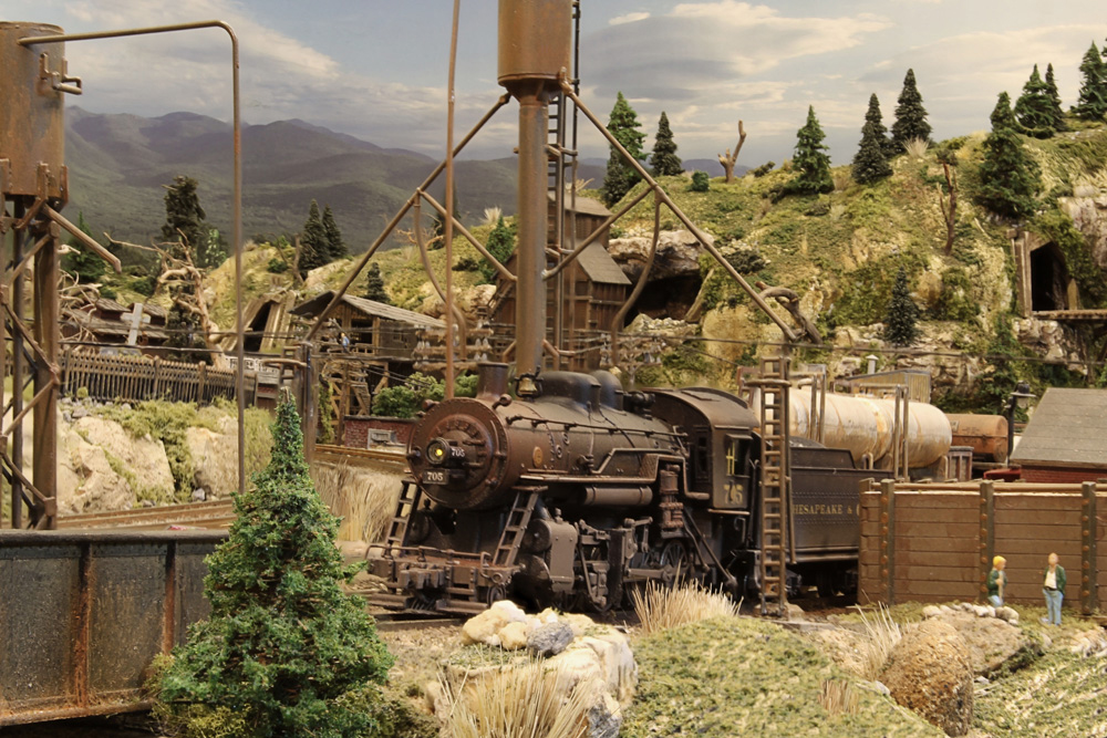 A weathered 2-8-0 steam locomotive rests in the engine servicing area while its crew takes a break