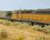 : A rusty yellow-and-green diesel and a worn green covered hopper roll down an equally neglected spur track on the prairie