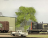 A black-and-red Canadian National switcher backs toward a brown CN boxcar in front of a corrugated metal building