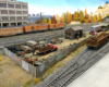 Wood fence encloses junkyard with red stakebed truck and corrugated steel office, rusty gondola spotted at siding