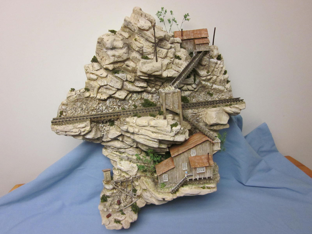 A wall sculpture depicts a sheer cliff face with an HO scale track and several mining buildings clinging to it