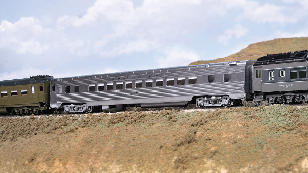 An HO scale passenger car with a shiny silver finish coupled between two other cars.