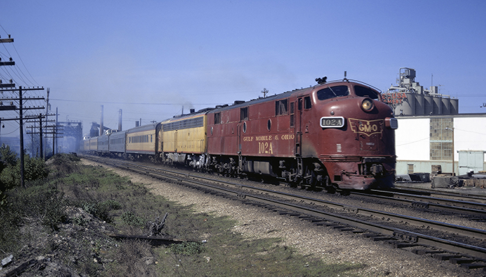 Red and yellow locomotives leading passenger train with cars of several colors.