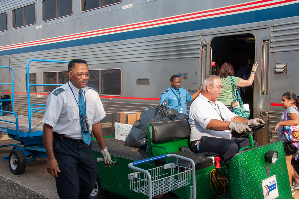 Amtrak employee handling baggage next to train.