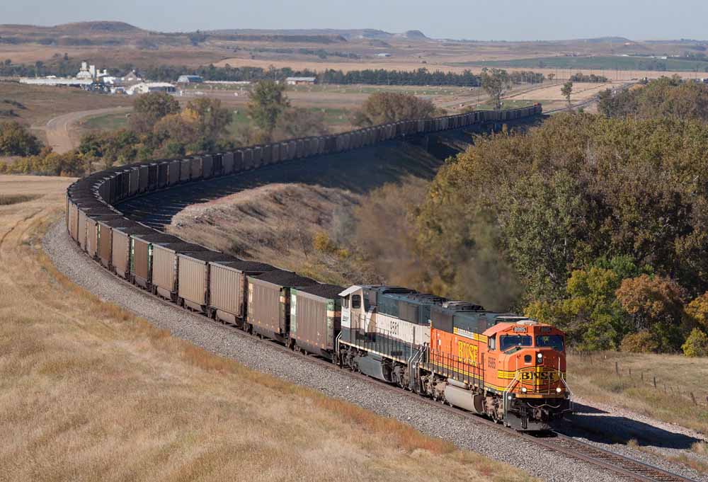 Diesel locomotives power a coal train around bend in rolling hills