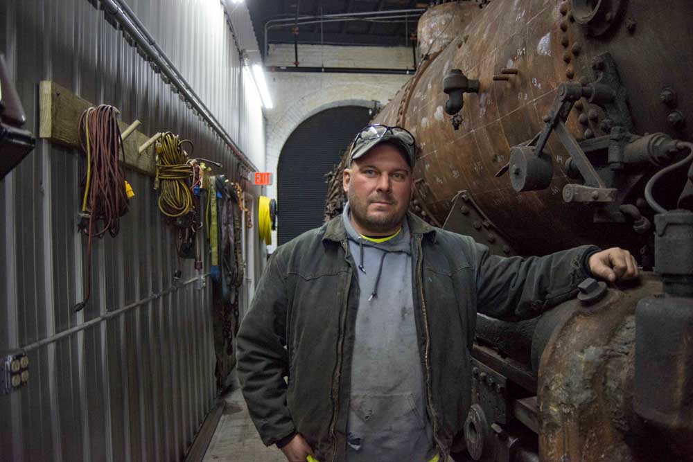 Man standing beside steam locomotive boiler in shop