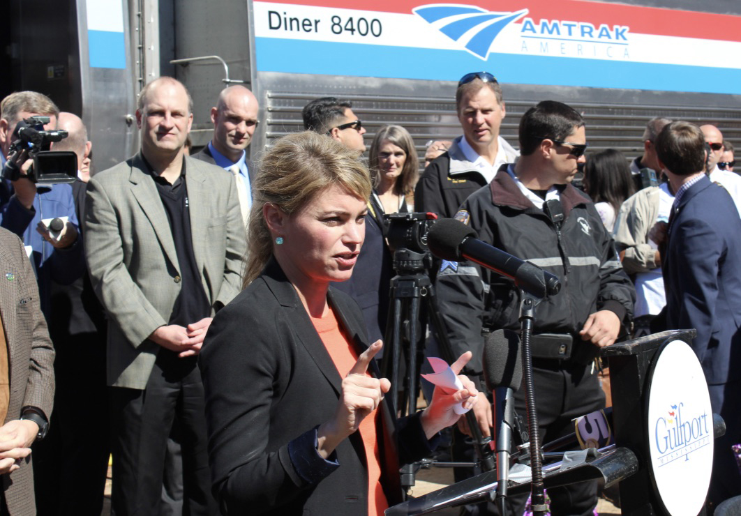 Woman speaking in crowd in front of passenger train