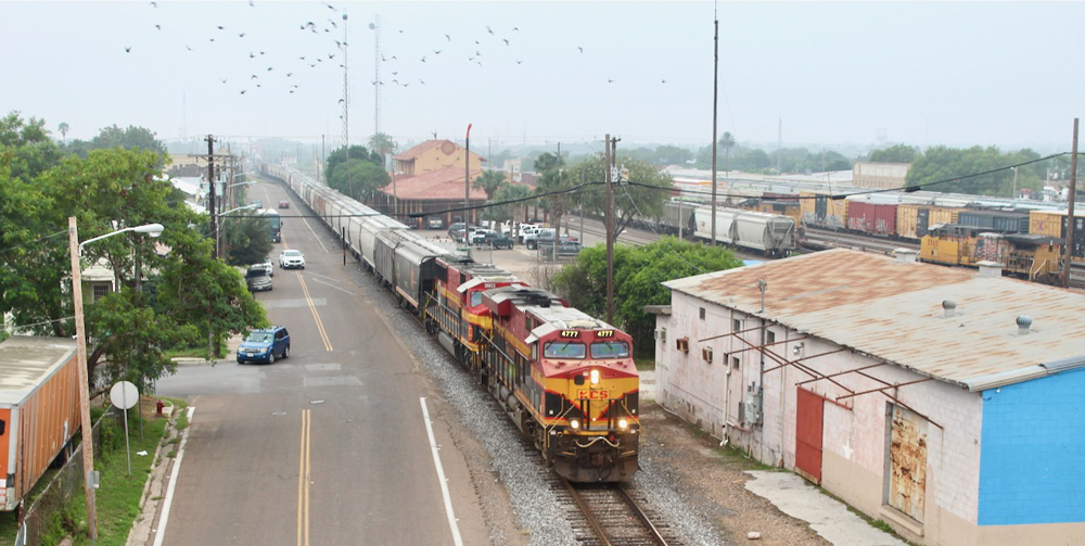 Train with two locomotives and hopper cars on track parallelling street