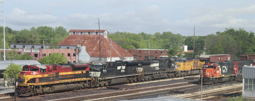 Train with Kansas City Southern, Norfolk Southern, and Union Pacific locomotives passes one with Canadian Naitonal power