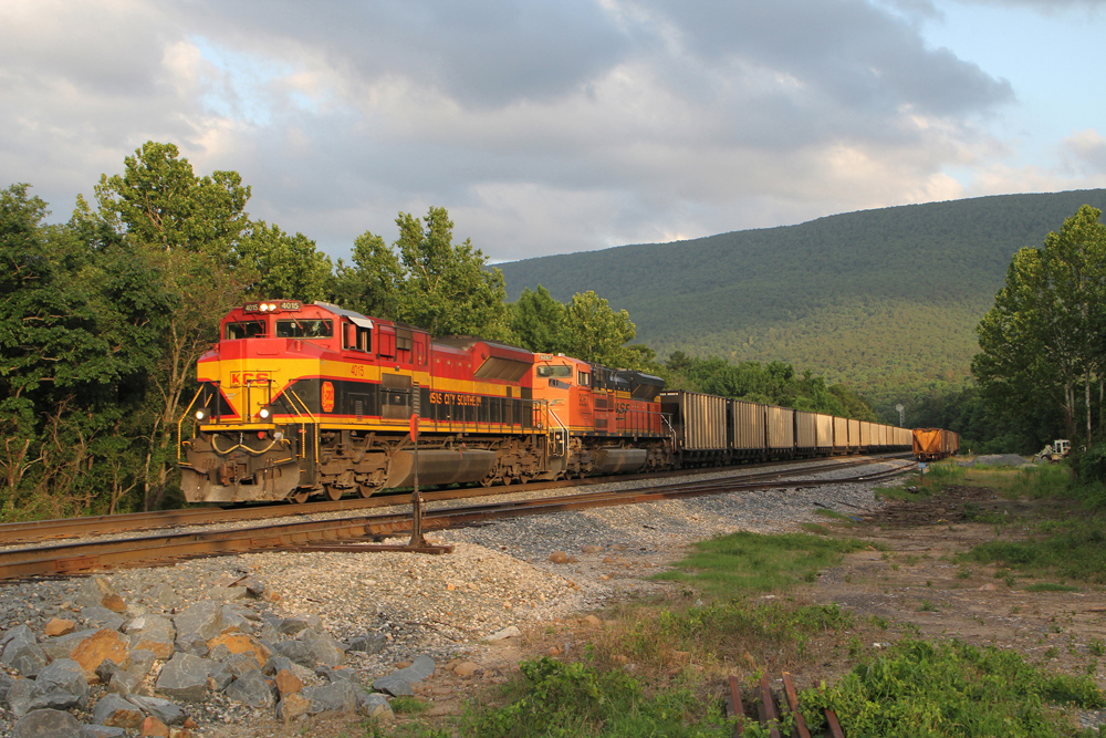 KCS and BNSF engines lead coal train with mountain in distance.