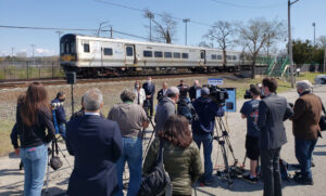 Reporters surrounding officials at press conference with train in background